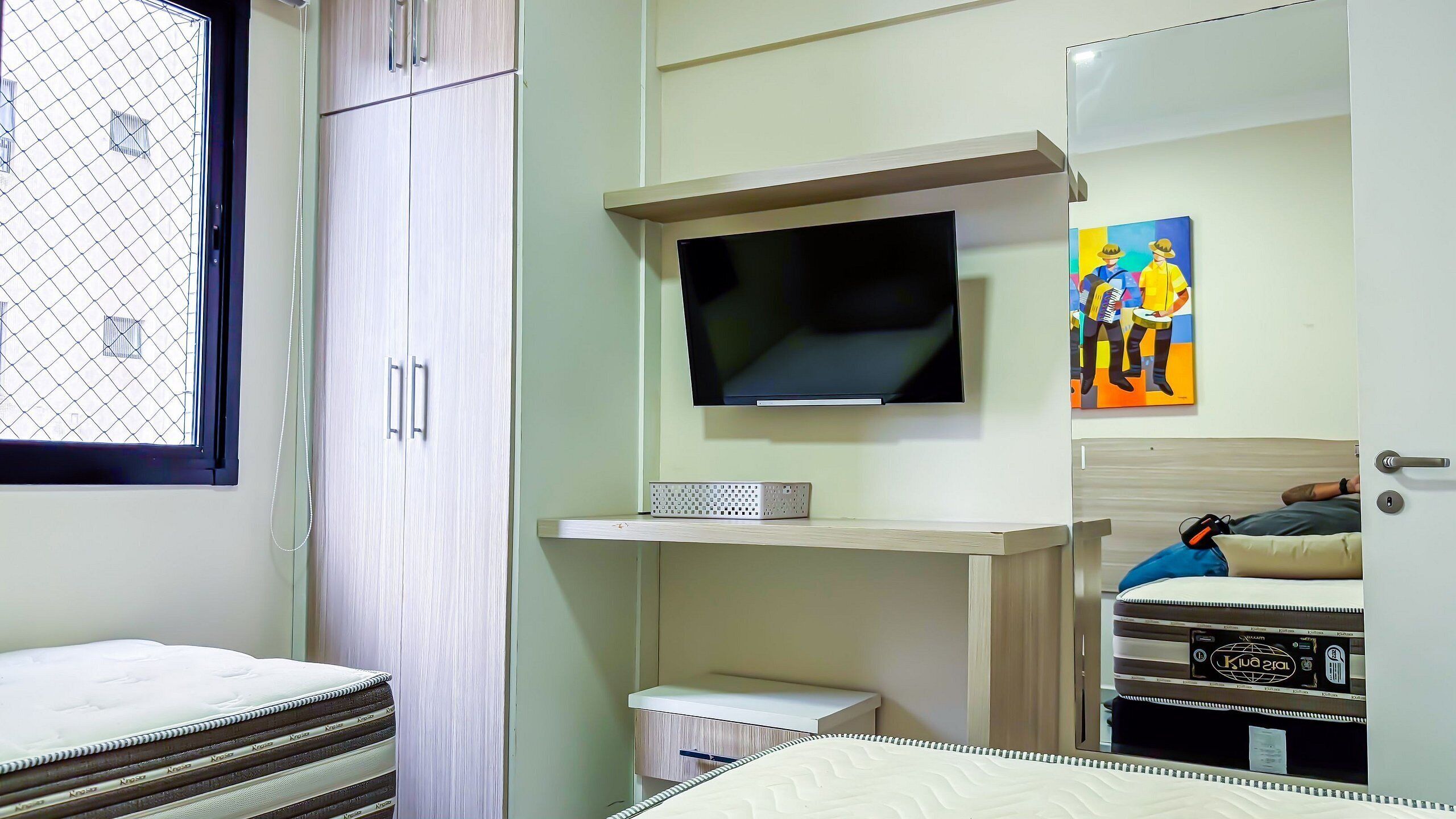 A bedroom with a bed, a TV, a small desk, and a wardrobe.