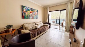 Ein Wohnzimmer mit einer Couch, einem Couchtisch, einem Fernseher und einem Balkon mit Blick.
