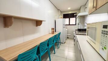 Una cocina con una mesa de madera, sillas color turquesa, armarios blancos, un refrigerador y un microondas.