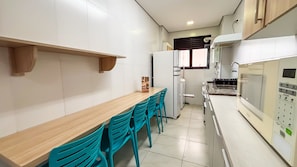 A kitchen with a wooden table, teal chairs, white cabinets, a refrigerator, and a microwave. - SHB Lazer Completo 2min da Praia (Guarujá)