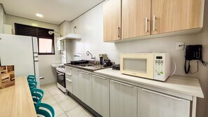A compact kitchen with a gas stove, microwave, and a phone on the wall. - SHB Lazer Completo 2min da Praia (Guarujá)