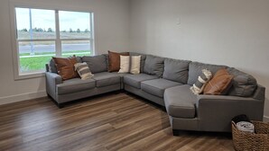 A modern living room with a sectional sofa, a large window, and a view of a green landscape. - Ash & Alder Townhouse (Idaho Falls)