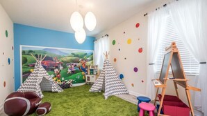 Lasten leikkihuone, jossa on seinämaalaus, teepeitä, jalkapallo ja maalausteline.