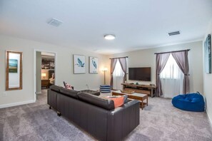 A living room with a sofa, a television, a coffee table, and a bean bag. - 6BR ChampionsGate Villa with Pool & Game Room (Kissimmee)