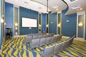 A conference room with a large screen, rows of chairs, and a patterned carpet. - 6BR ChampionsGate Villa with Pool & Game Room (Kissimmee)