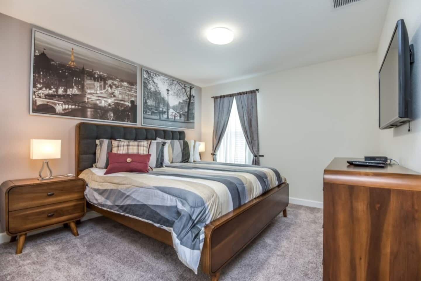 A bedroom with a bed, nightstands, a dresser, a flat-screen TV, and two large framed pictures on the wall.