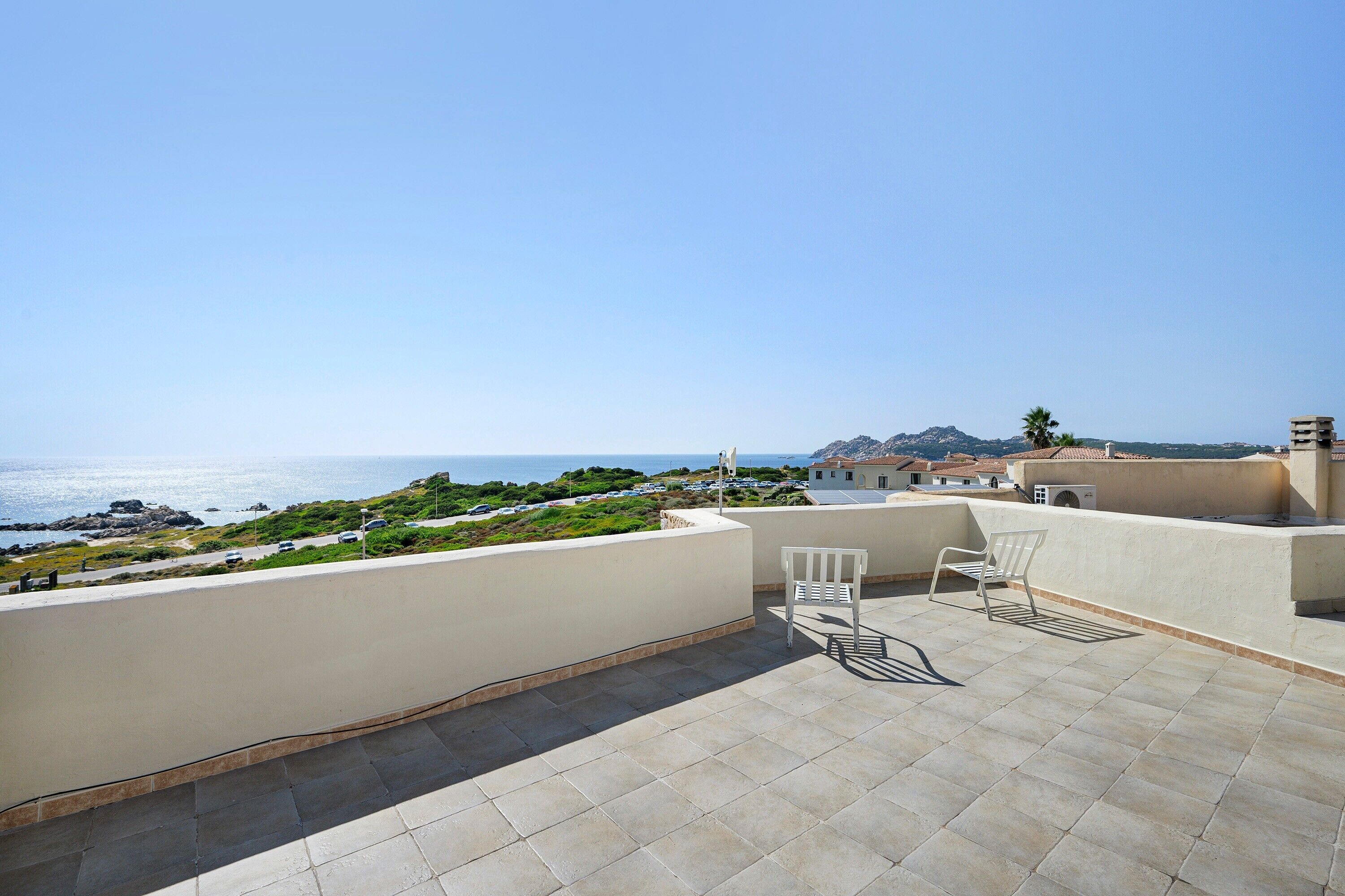 Une terrasse sur le toit avec vue sur la mer, une chaise blanche et une petite table.