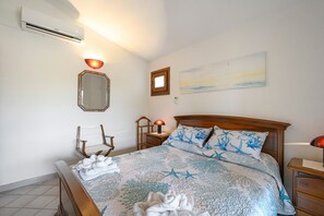 Une chambre à coucher comprenant un lit, une table de chevet, une chaise, un miroir, une lampe fixée au mur et un tableau.