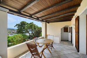 Un espace extérieur abrité, équipé d’une table et de chaises, offrant une vue sur le paysage, et une porte donnant accès à une salle de bain.