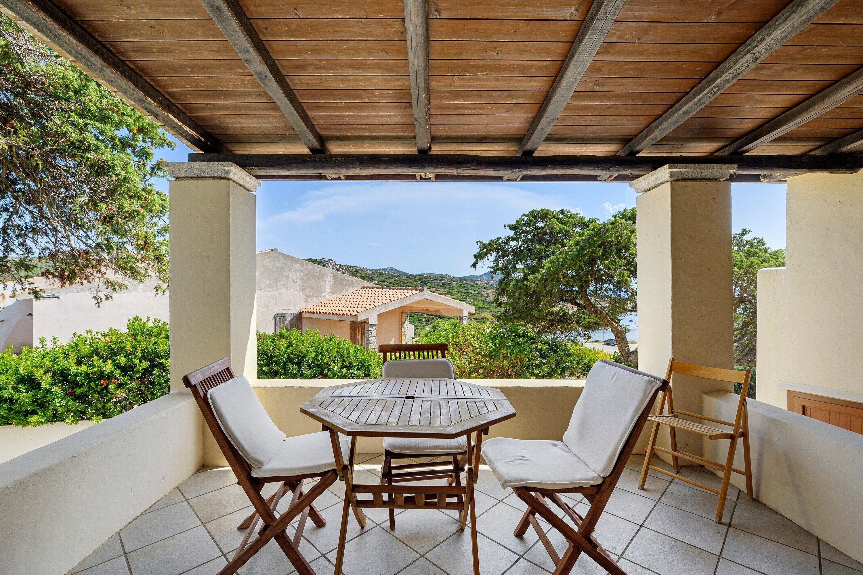 Un espace extérieur abrité, aménagé avec une table et des chaises, offrant une vue panoramique sur un paysage pittoresque composé de collines et d’un bâtiment situé au loin.