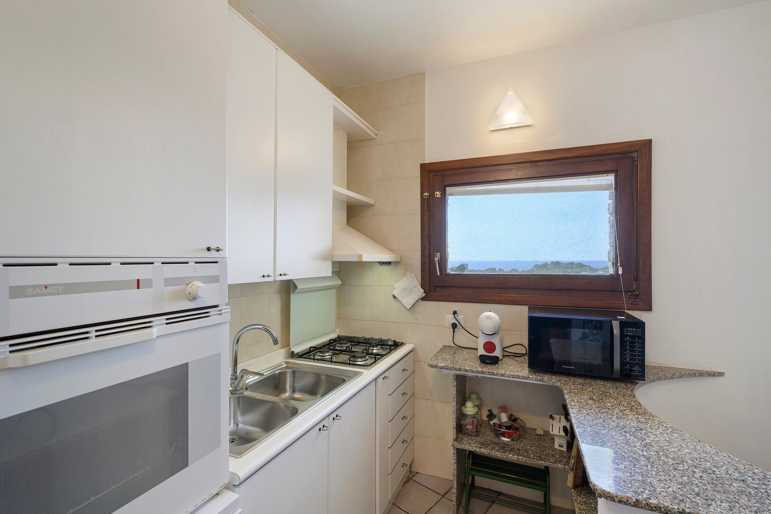 Cocina compacta con armarios blancos, cocina a gas, un lavamanos y una ventana con vistas.