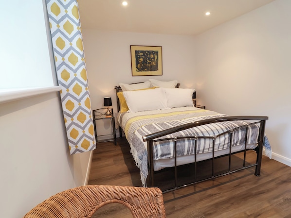 A bedroom with a bed, bedside tables, a lamp, a framed picture on the wall, and a patterned curtain.