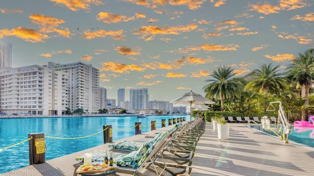 A poolside area with lounge chairs, a dining table with food, and a view of high-rise buildings. - Intracoastal View Apt - Resort Amenities & Pool (Hallandale Beach)