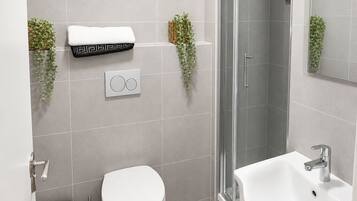 Et moderne badeværelse med toilet, bidet, vask og bruseområde.