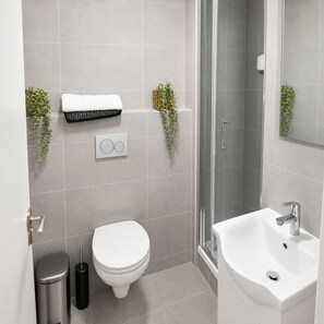 A modern bathroom with a toilet, bidet, sink, and a shower area.