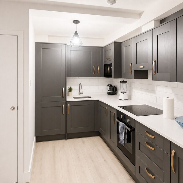 A modern kitchen with dark grey cabinets, a white countertop, a stainless steel sink, a coffee maker, and a black stove.