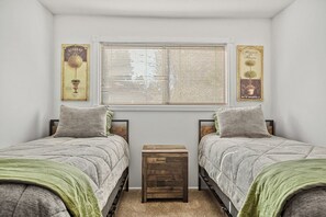 Une chambre avec deux lits, une fenêtre avec des stores et des œuvres d’art décoratives au mur.