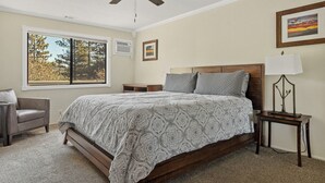 Una camera da letto con un letto, una sedia, un comodino, una lampada, una ventola a soffitto e una finestra vista alberi.