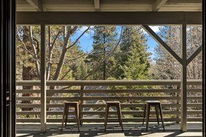 Un espace extérieur abrité, doté d’une rambarde en bois, de trois tabourets en bois et offrant une vue sur les arbres et le ciel.