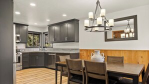 Una cucina moderna con mobili scuri, un tavolo da pranzo in legno e un lampadario.