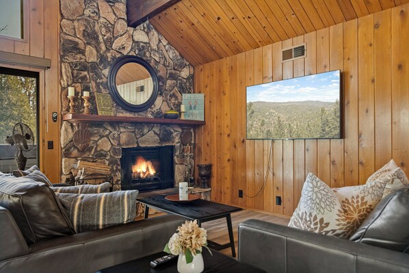 A cozy living room with a stone fireplace, leather sofas, and a large TV screen. - Quiet Mountain Cabin Escape (Lake Arrowhead)