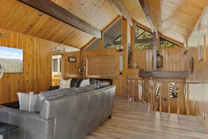 A cabin interior with a sofa, wooden walls, a kitchen area, and a view of the outdoors. - Quiet Mountain Cabin Escape (Lake Arrowhead)