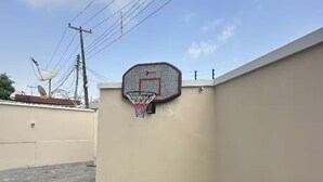 Un aro de baloncesto sujeto a una pared, con cables de electricidad y una antena parabólica al fondo.