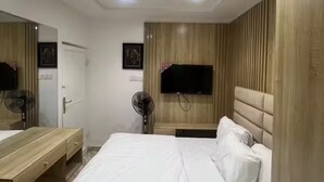 Un dormitorio con cama, mesitas de noche, televisor montado en la pared y un ventilador.