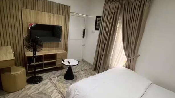 Habitación de hotel con cama, televisión montada en la pared, ventilador, mesita y puerta.