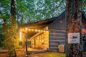 Una baita con un portico, luci a stringa e un cartello che indica 'Misty Mountain Cabin 2034 – Parcheggio Riservato'.