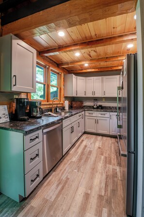 A modern kitchen with wooden ceiling beams, stainless steel appliances, and a large window. - Modern 2-bedroom cabin with Hot Tub in charming Pigeon Forge (Pigeon Forge)