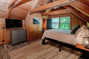 A wooden room with a bed, a television, a cabinet, and a window with a view of trees. - Modern 2-bedroom cabin with Hot Tub in charming Pigeon Forge (Pigeon Forge)