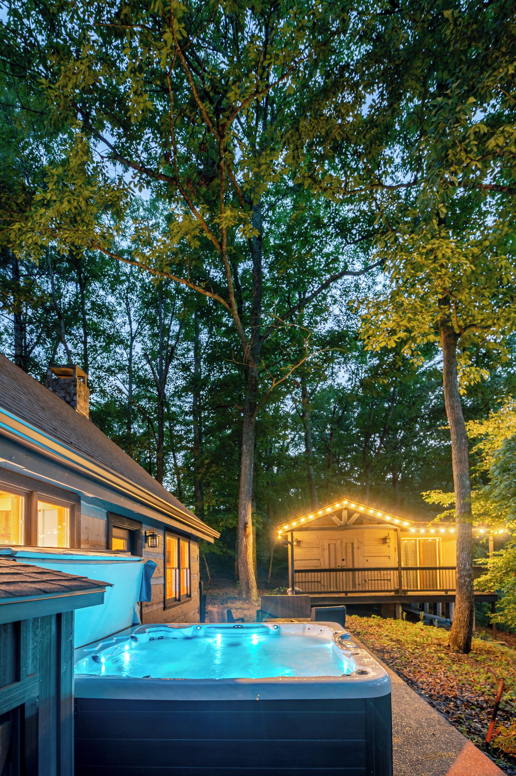 A hot tub in a wooded area with a house in the background.
