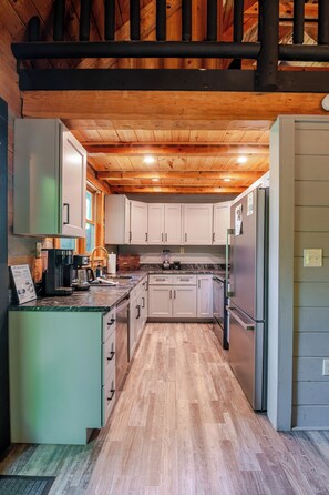 Cocina moderna con vigas de madera en el techo, armarios blancos y electrodomésticos de acero inoxidable.