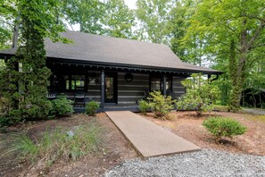 A cabin with a covered porch, a gravel driveway, and surrounding greenery. - Modern 2-bedroom cabin with Hot Tub in charming Pigeon Forge (Pigeon Forge)