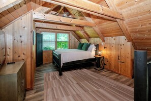 Ein Schlafzimmer im Dachgeschoss mit Holzboden, einem Bett, einem Nachttisch, einer Lampe und einem Kleiderschrank.