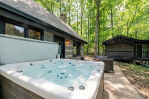 Ein Whirlpool vor einer Hütte mit einer Terrasse, umgeben von Bäumen.
