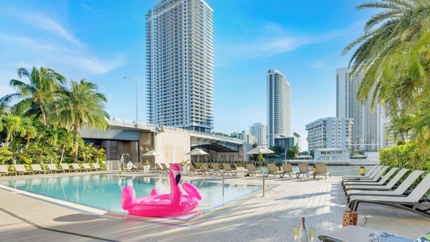 A pool area with lounge chairs, a pink flamingo float, and tall buildings in the background. - Beachwalk Studio Resort-Style Amenities (Hallandale Beach)