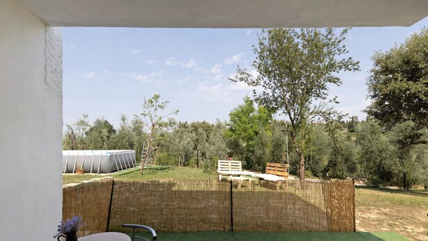 Un patio con mesa y sillas, cercado por una valla de madera, y vistas a un área verde con árboles.