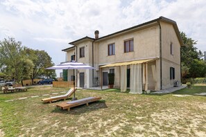 Ein zweistöckiges Haus mit einer Terrasse, Gartenmöbeln und einer überdachten Sitzgelegenheit.