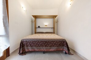 A narrow room with a bed, a mirror, and a shelf with a lamp. - Apartment 'Mini Cielo' with Shared Garden, Wi-Fi and Air Conditioning (Volterra)