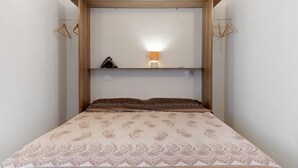 Una cama con una colcha estampada, una lámpara de noche y una estantería con un objeto pequeño.