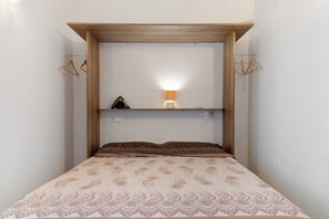 Ein Bett mit einem gemusterten Überwurf, einer Nachttischlampe und einem Regal mit einem kleinen Gegenstand.