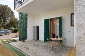 A small outdoor area with a stone floor, a table with two chairs, a refrigerator, and a door with green shutters. - Apartment 'Mini Cielo' with Shared Garden, Wi-Fi and Air Conditioning (Volterra)