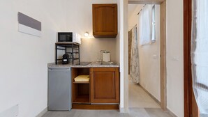 Una cocina compacta con microondas integrado, un refrigerador pequeño y armarios de madera.