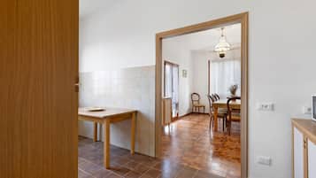 Ein Zimmer mit Holztür, einem Esstisch mit Stühlen, einer Küchenzeile mit Fliesenwand und einem Flur, der in ein weiteres Zimmer führt.