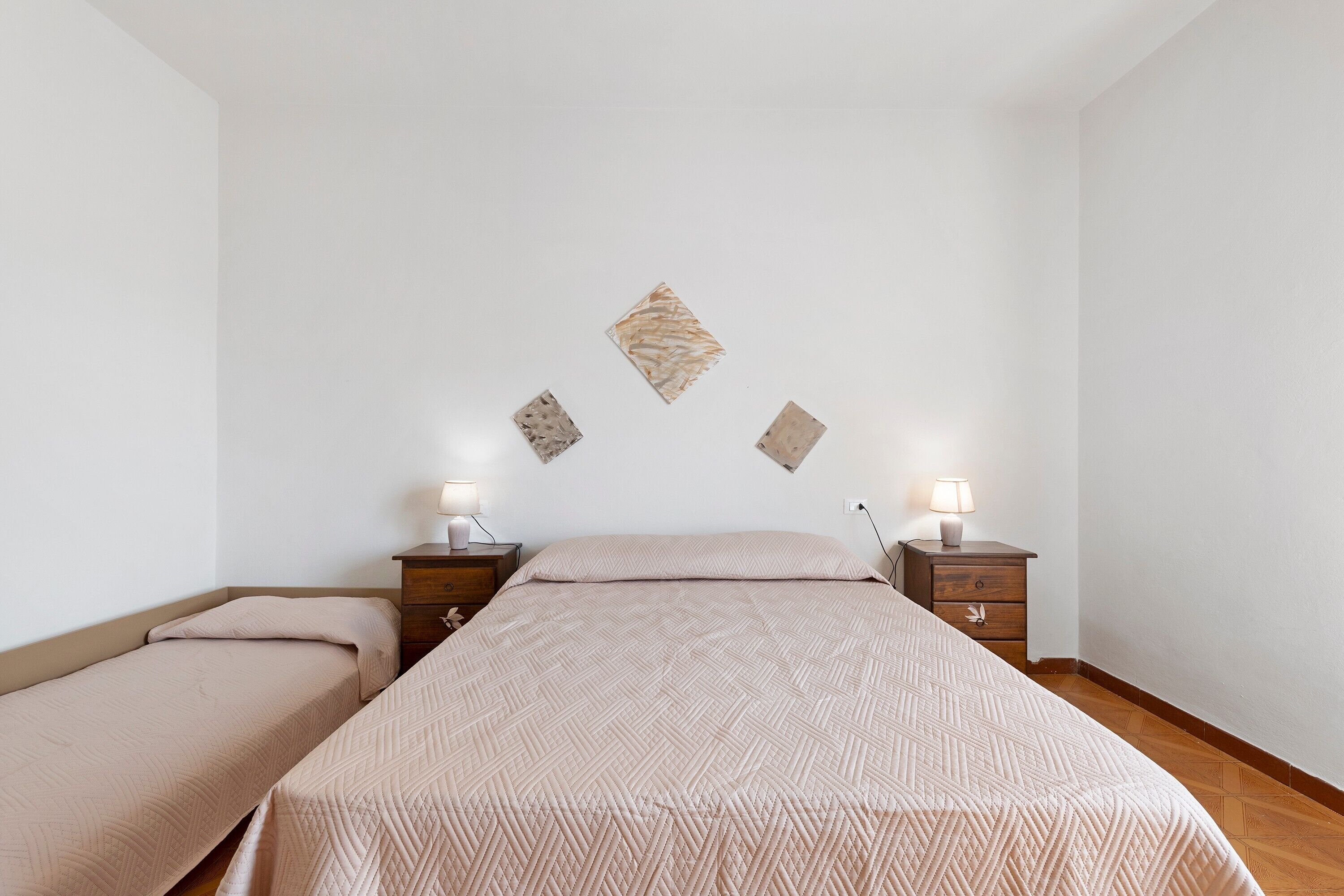 A bedroom with two beds, a nightstand with a lamp, and decorative wall art.