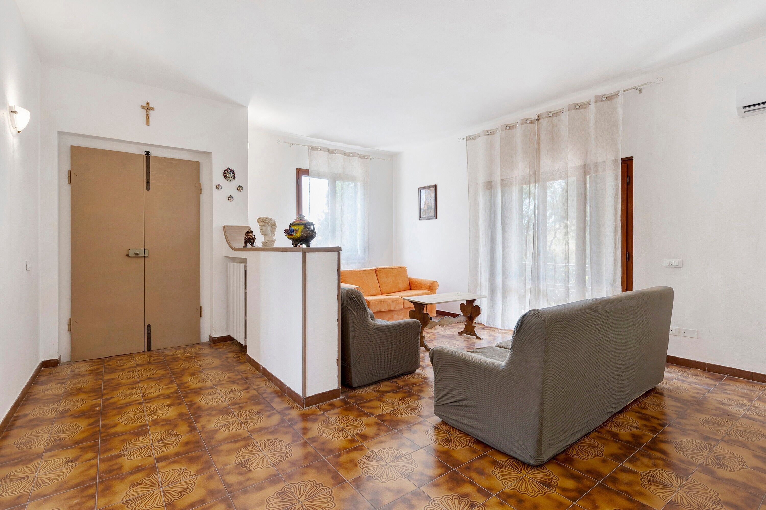 Una habitación con un sofá, dos sillones, una mesita, un jarrón decorativo y una cruz en la pared.