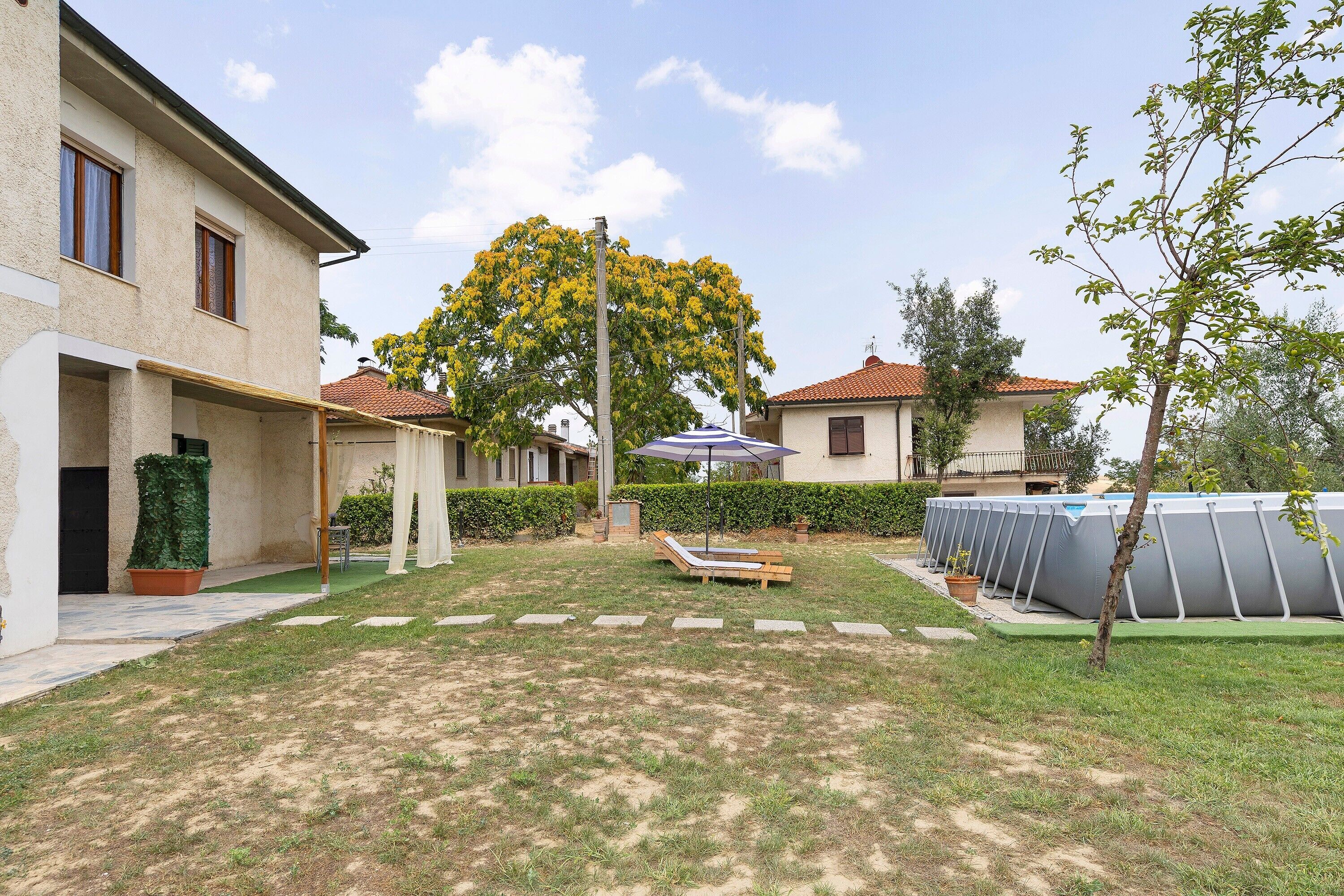 A residential area with a grassy lawn, a swimming pool, and a tree with yellow flowers.