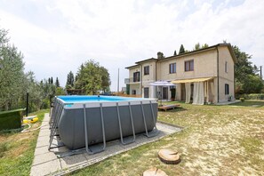 Ein Wohnhaus mit Swimmingpool, überdachter Terrasse und einem großen Gebäude mit vielen Fenstern.